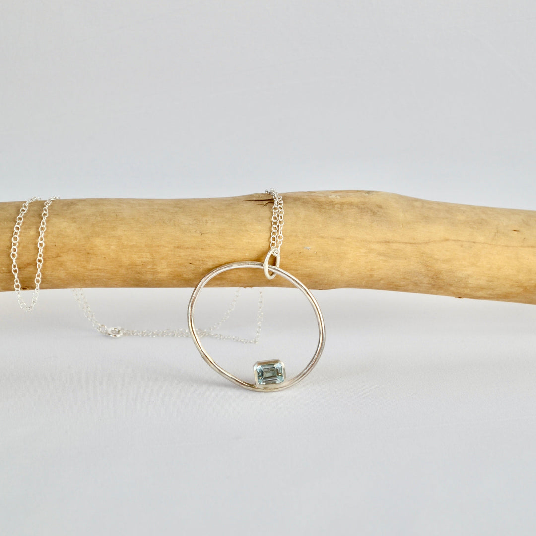 Silver hoop necklace on a wooden stick with a white background