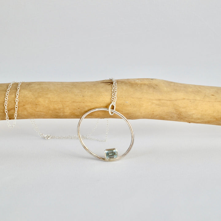 Silver hoop necklace on a wooden stick with a white background