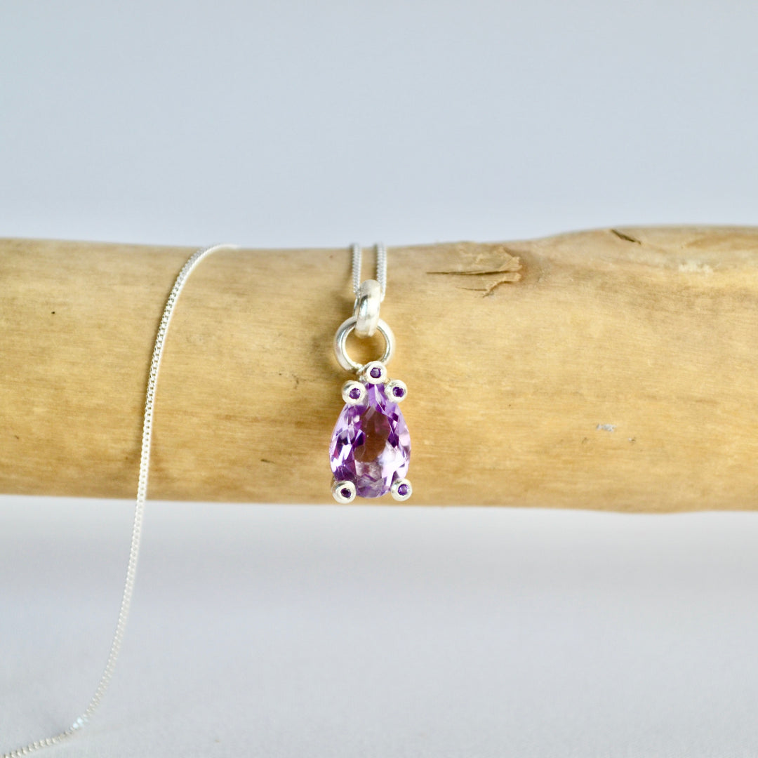 Amethyst pendant on a silver chain draped over wooden logs with a white background