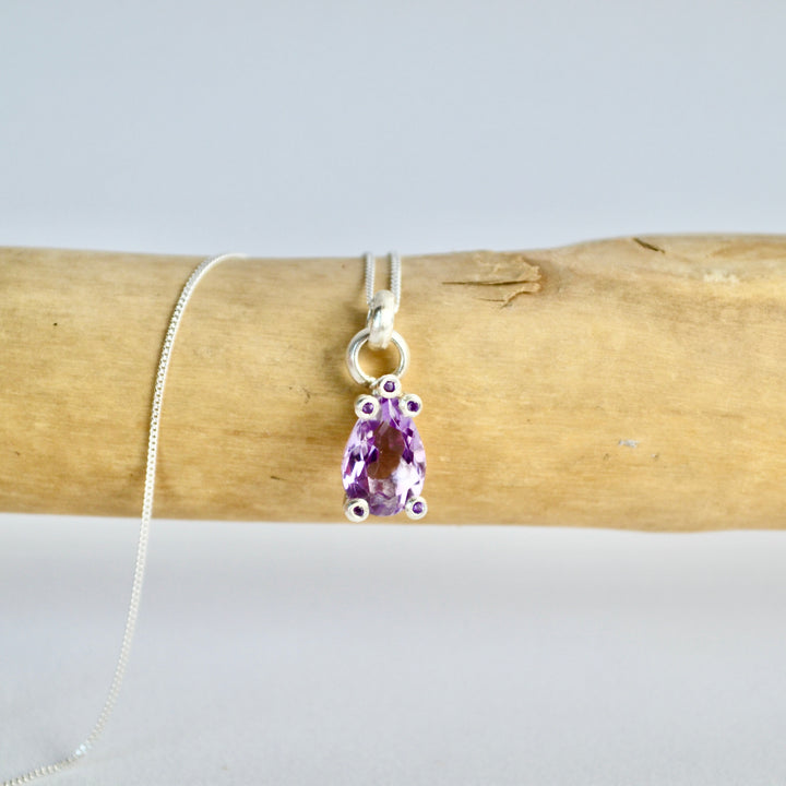 Amethyst pendant on a silver chain draped over wooden logs with a white background