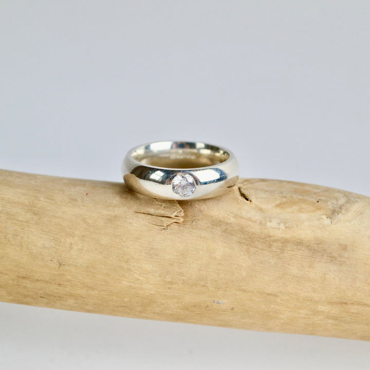 Silver ring with a diamond on a wooden branch against a gray background