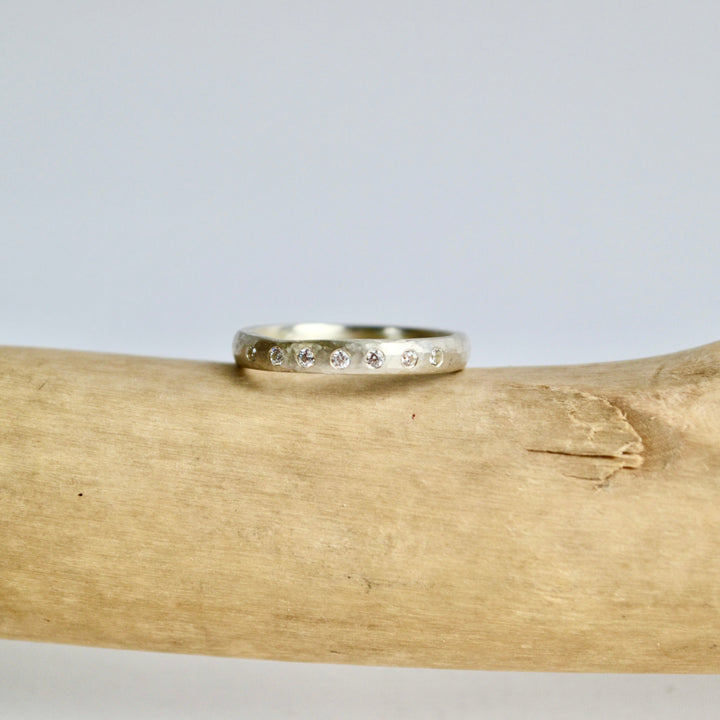 Silver ring with engraved text on a wooden log against a gray background