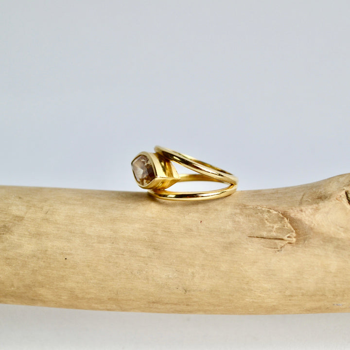 Gold ring with a gemstone on a piece of driftwood against a light gray background