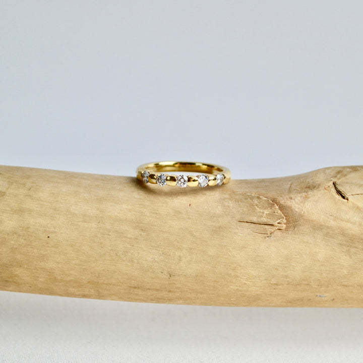 Gold ring with small diamonds on a wooden log against a light gray background