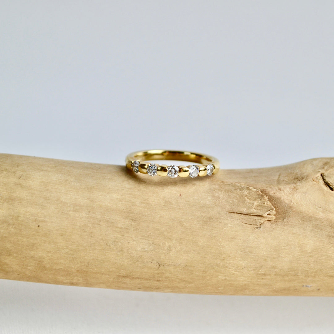 Gold ring with small diamonds on a piece of driftwood against a light gray background