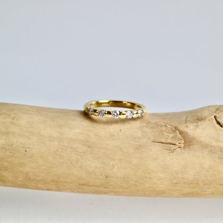 Gold ring with small diamonds on a piece of driftwood against a light gray background