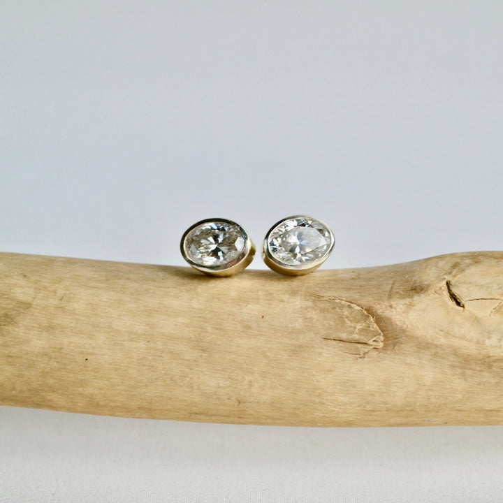 Gold stud earrings with clear gemstones on a piece of driftwood against a light gray background