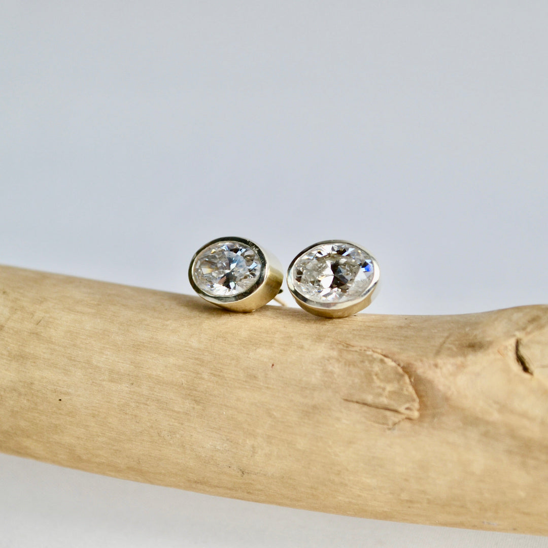 Pair of gold earrings with clear gemstones on a piece of driftwood against a light gray background