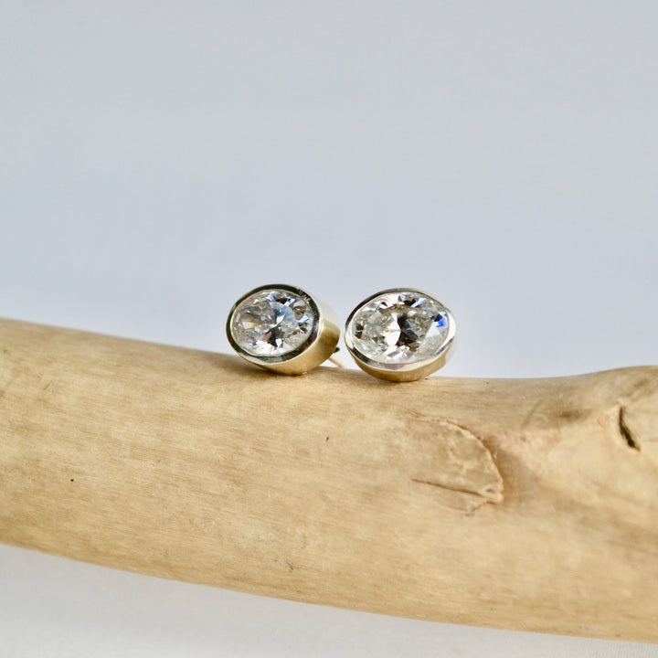 Pair of gold earrings with clear gemstones on a piece of driftwood against a light gray background