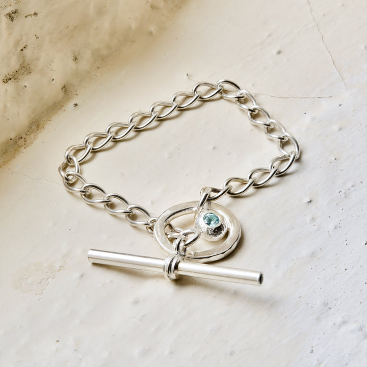 A sterling silver bracelet with a central topaz set within a circular frame, and a T-bar with a smaller topaz pendant.