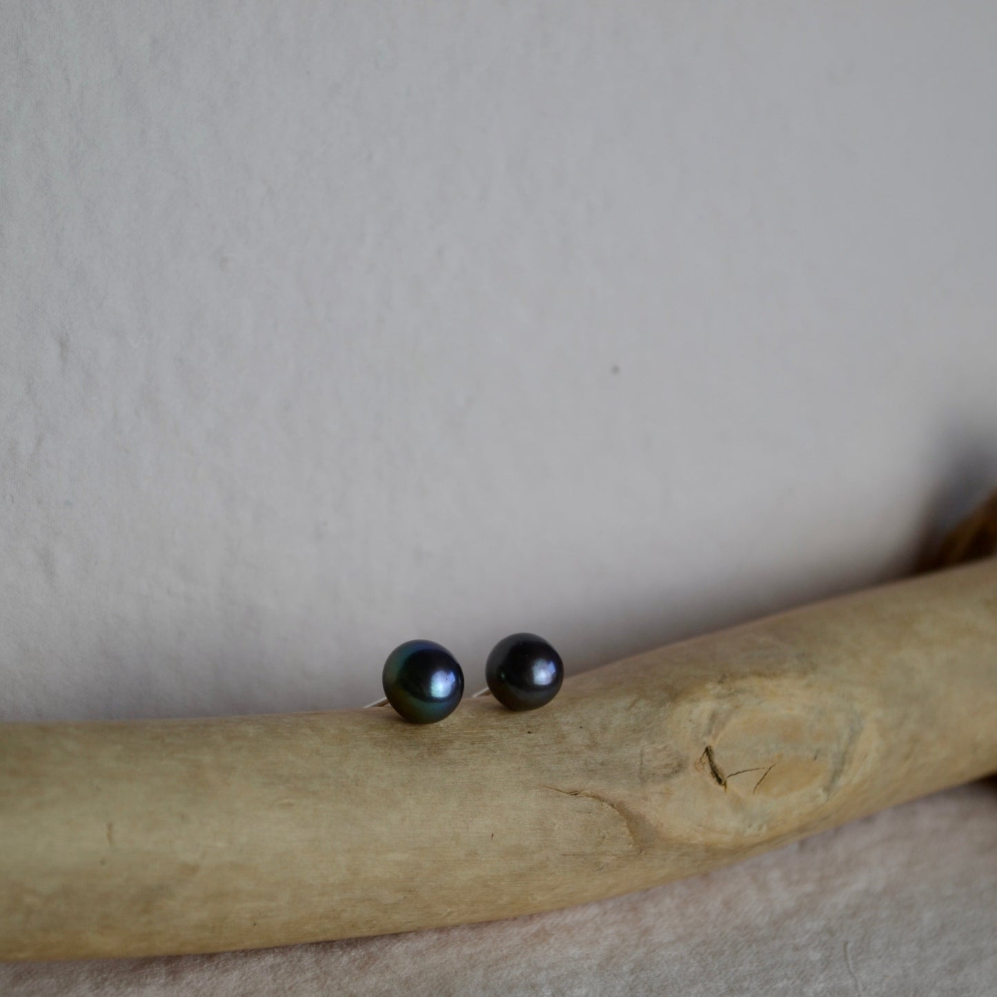 Black stud earrings on a piece of beige fabric with a neutral background