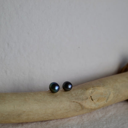 Black stud earrings on a piece of beige fabric with a neutral background