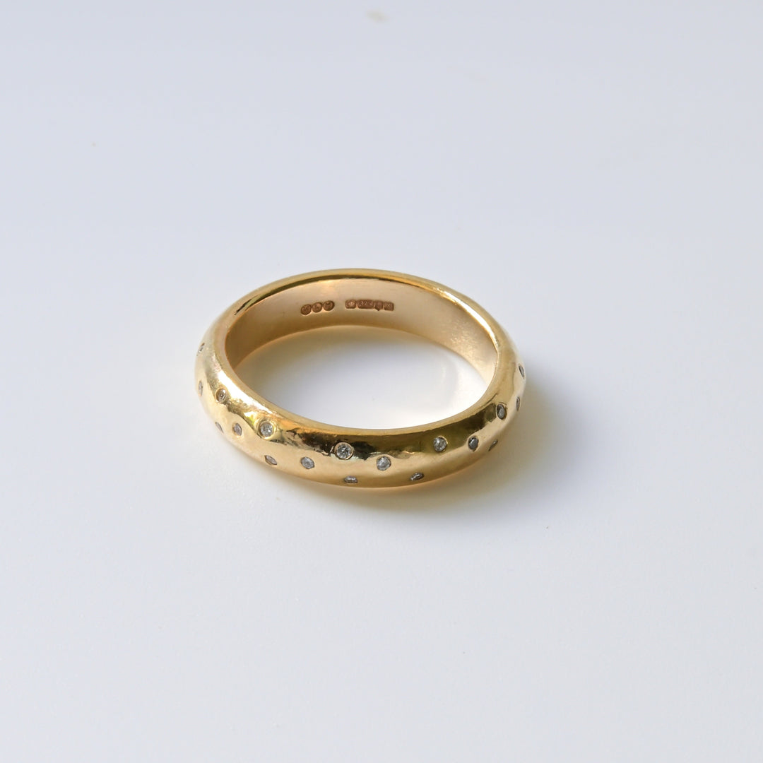 A close-up image of a gold wedding band with embedded white diamonds, showing the band&