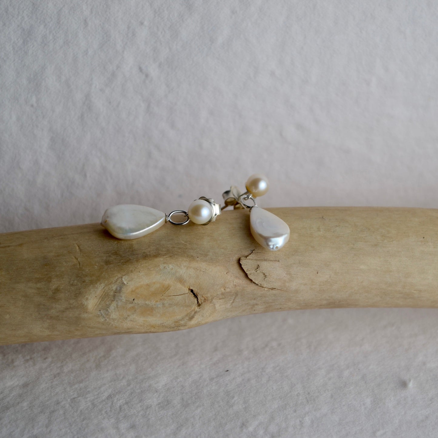 Pearl necklace with heart and teardrop pendants on a piece of driftwood against a plain background