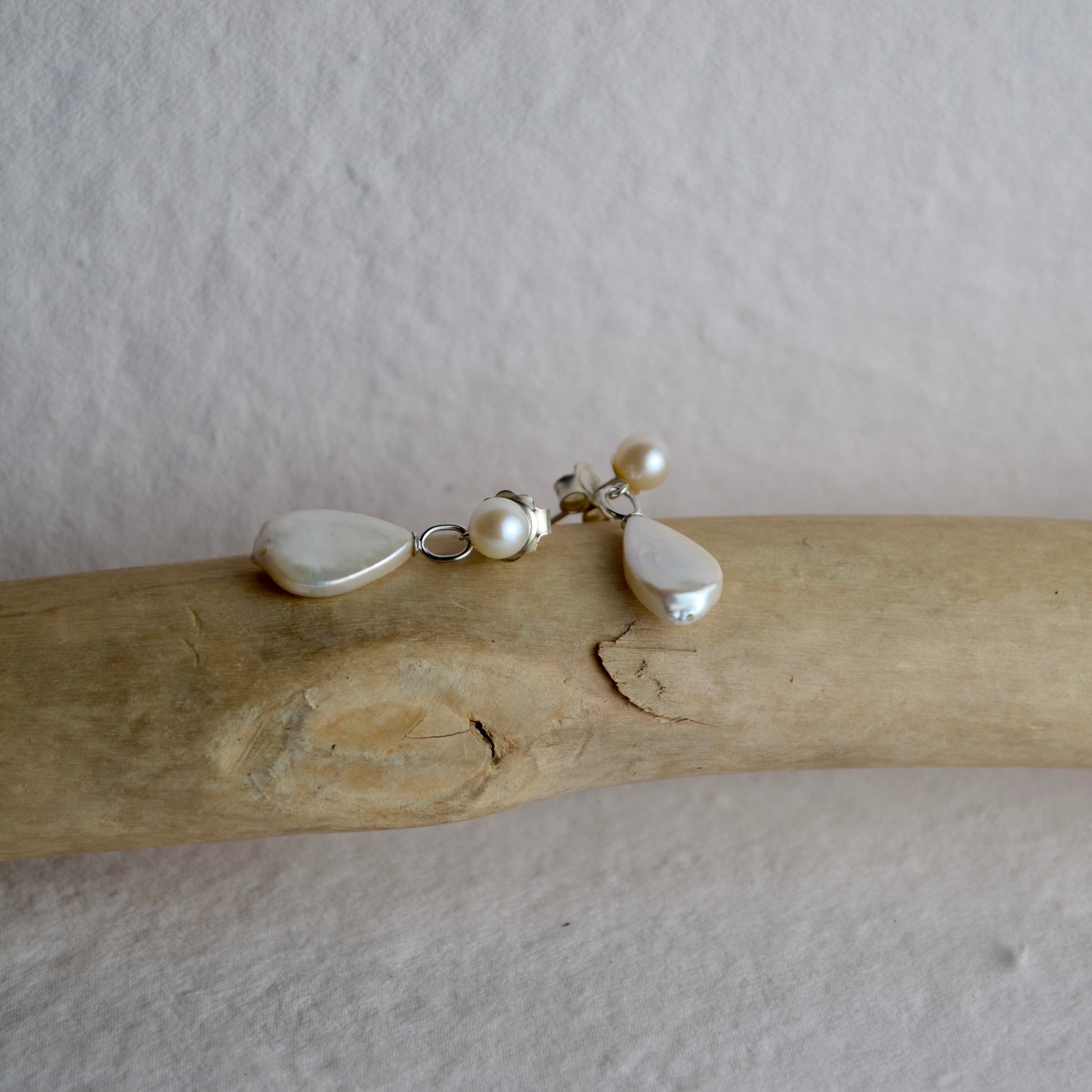 Pearl necklace with heart and teardrop pendants on a piece of driftwood against a plain background