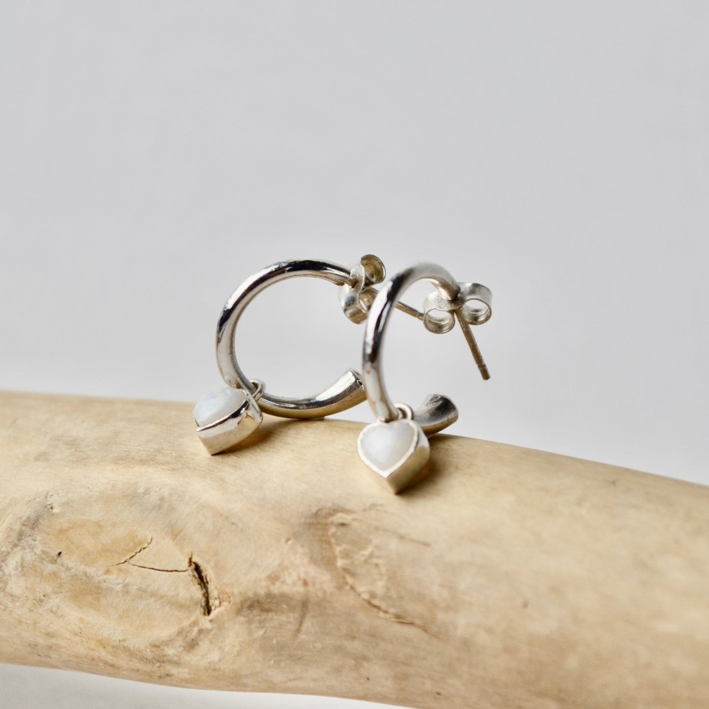 Silver hoop earrings with heart charms on a piece of driftwood against a light background