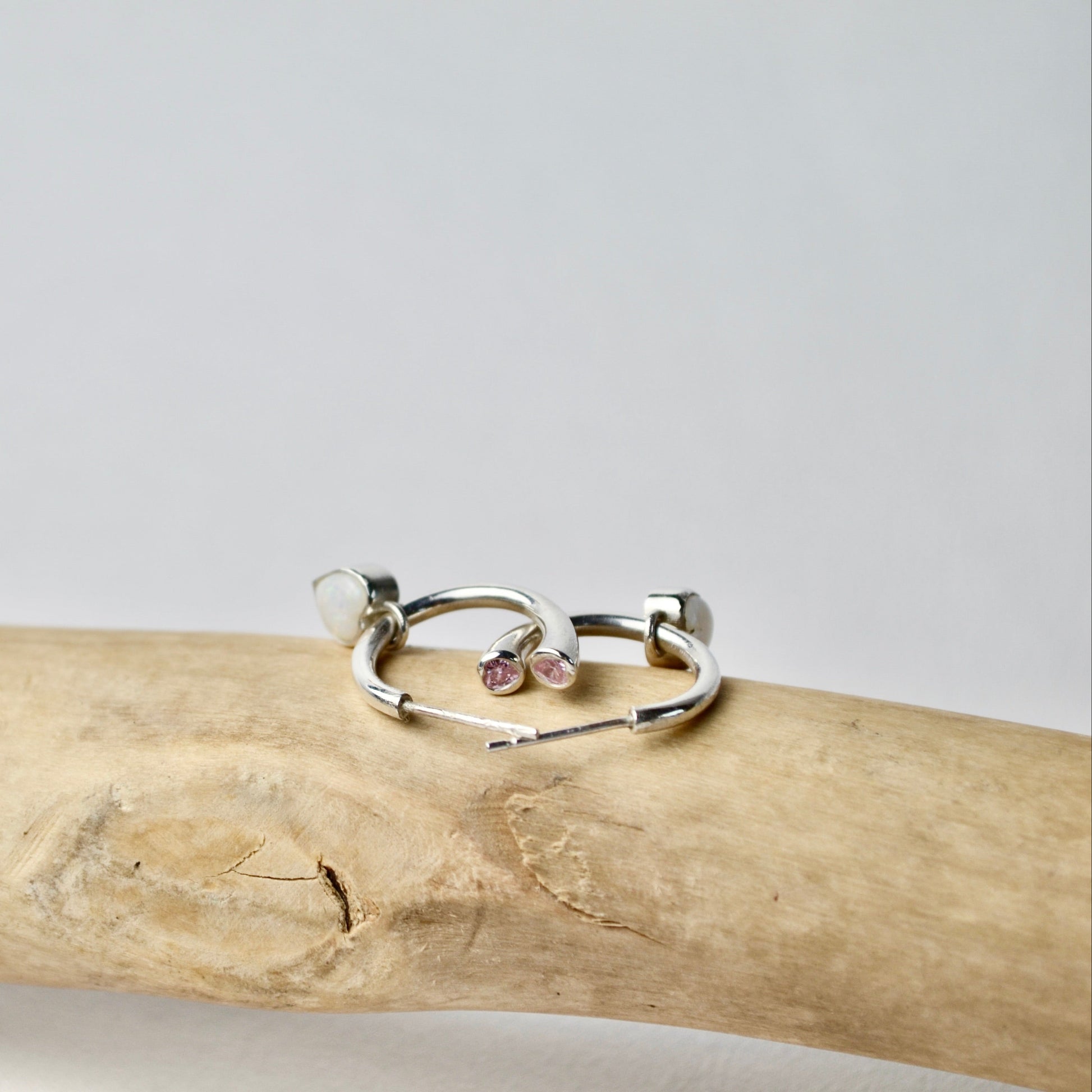 Two silver rings with small stones on a wooden stick against a light gray background