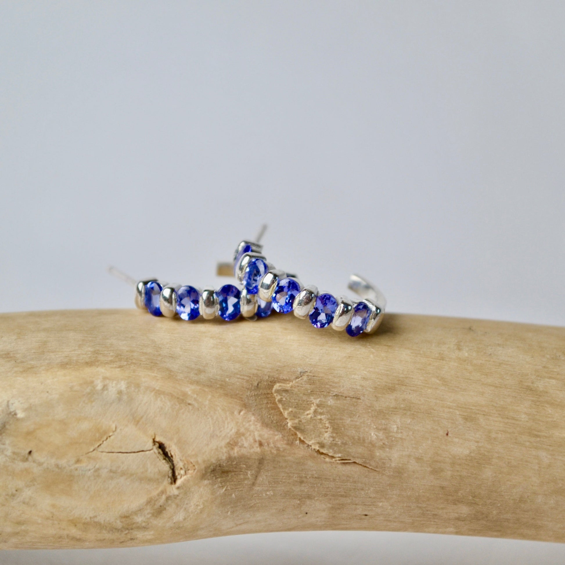Bracelet with blue and silver beads on a piece of driftwood against a light gray background