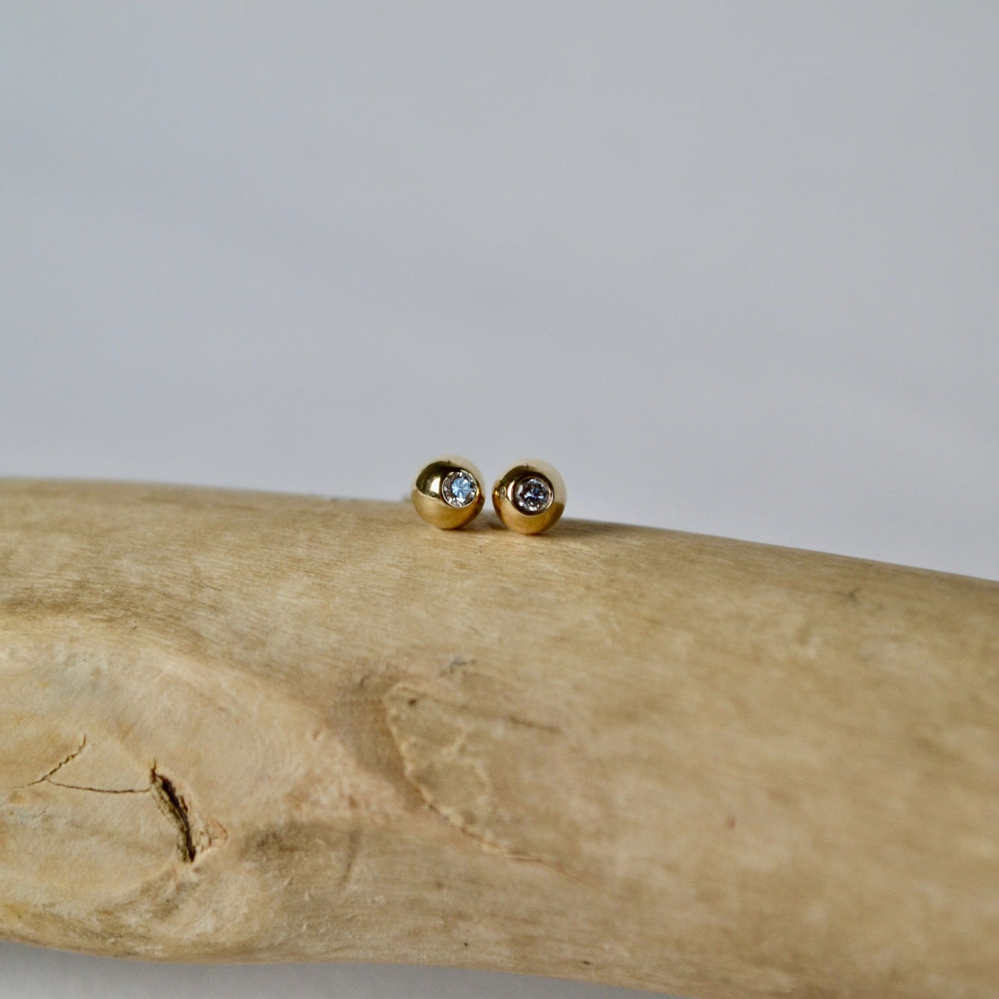 Gold earrings with gemstones on a piece of driftwood against a light background