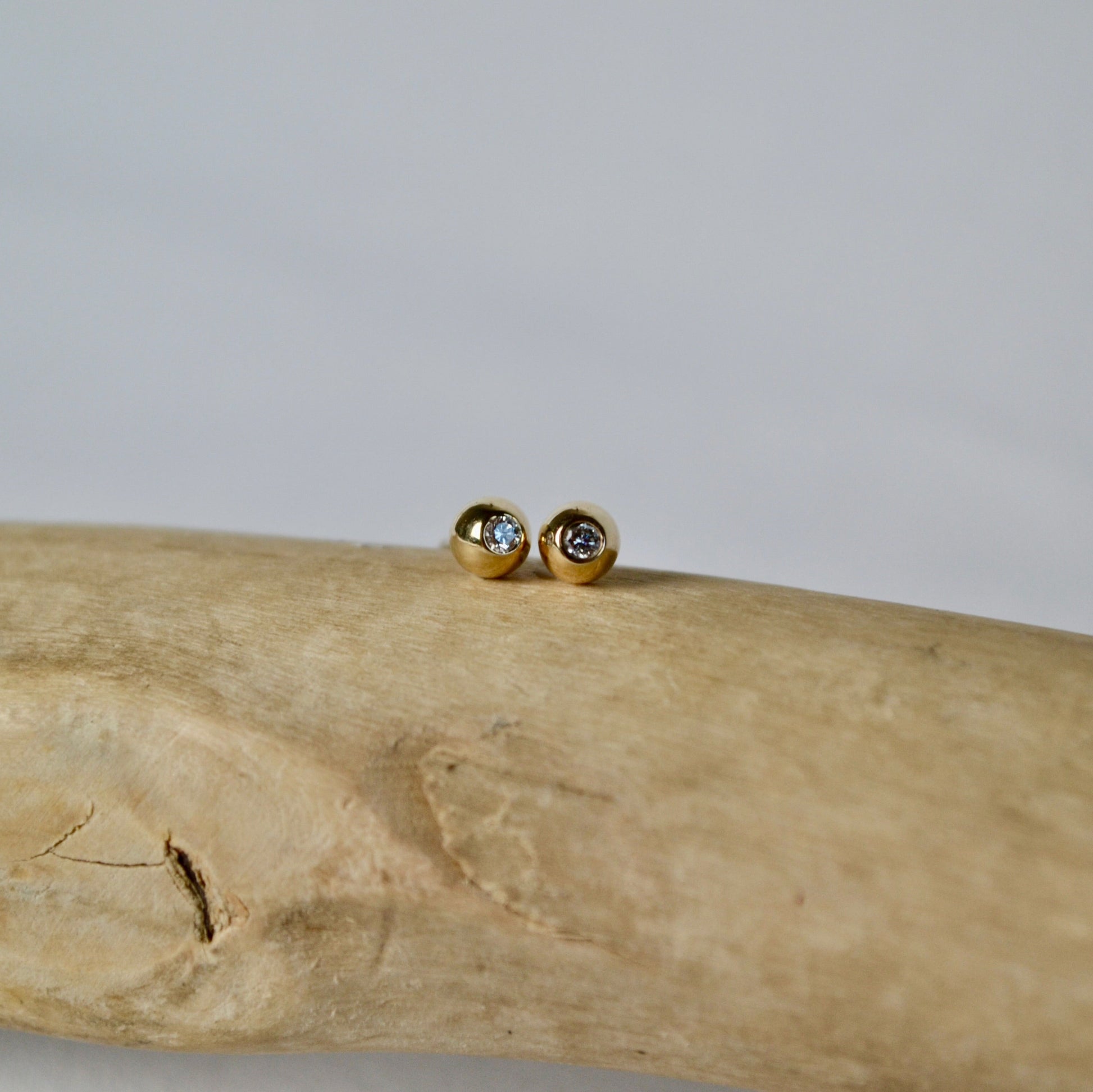Gold earrings with gemstones on a piece of driftwood against a light background