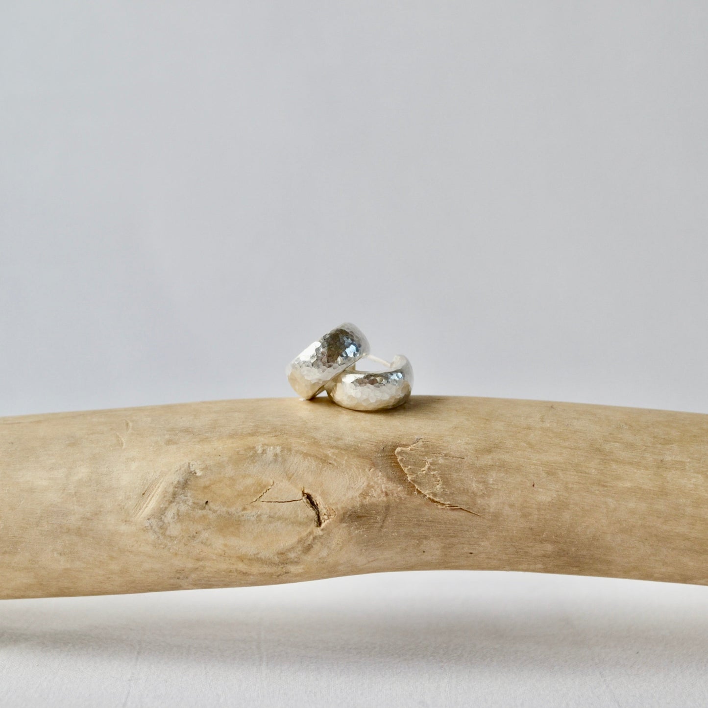 Two silver rings on a piece of driftwood with a plain background