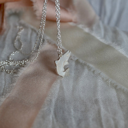 Silver necklace with a salmon pendant on a light fabric background