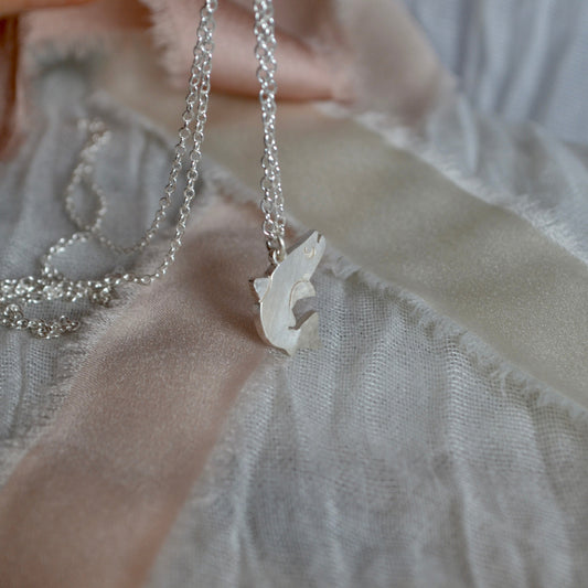 Silver necklace with a salmon pendant on a light fabric background