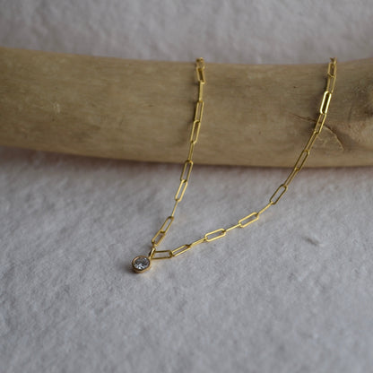 Gold chain necklace with a small pendant on a wooden stick against a light background