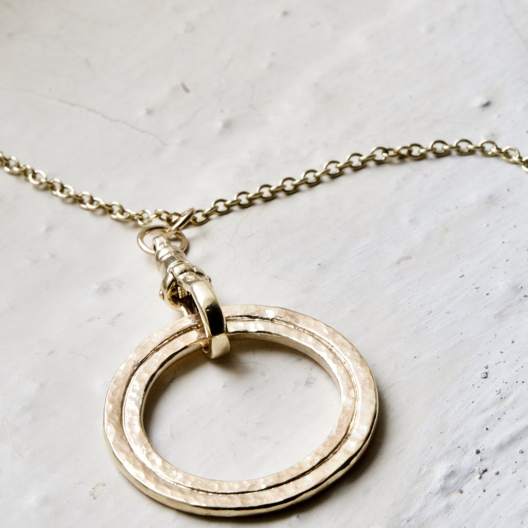 A gold necklace featuring a layered circle pendant, suspended from a curb chain.