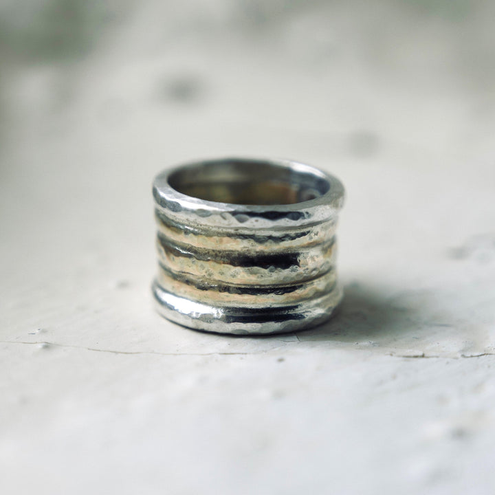 A chunky silver and gold ring with a textured surface, featuring three stacked bands of gold and two bands of silver on a rustic stone background.