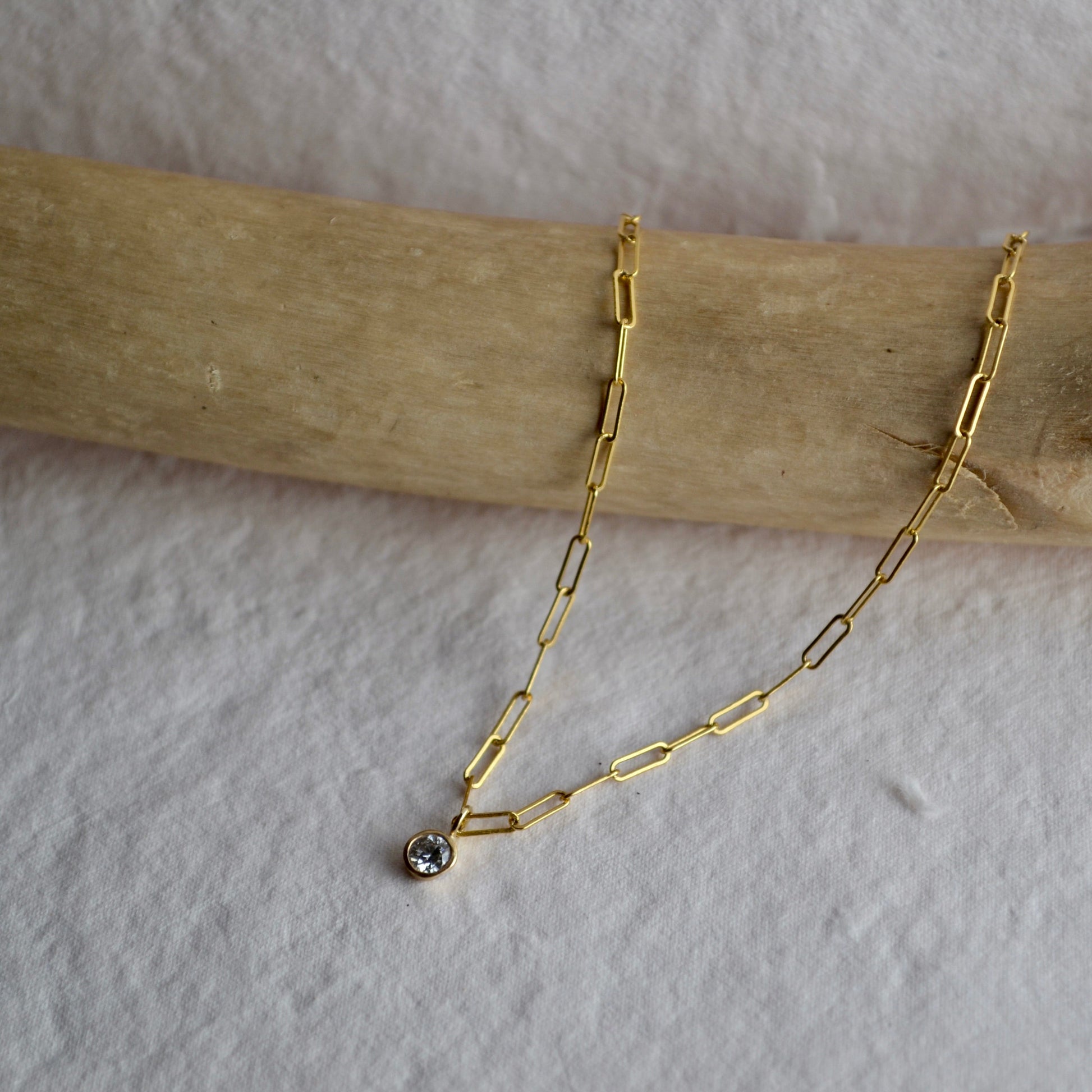 Gold chain necklace with a small pendant on a wooden stick against a white background