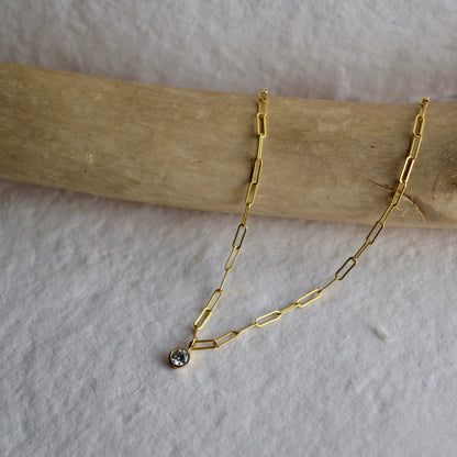 Gold chain necklace with a small pendant on a wooden stick against a white background