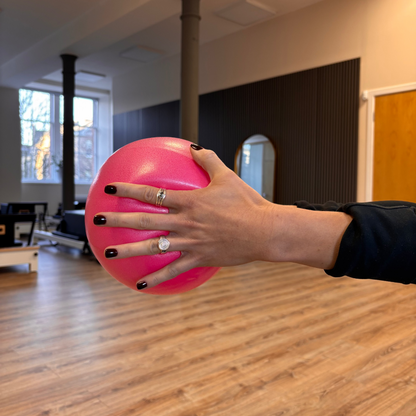 Hand holding a pink ball in an indoor setting with wooden flooring and a neutral color palette.