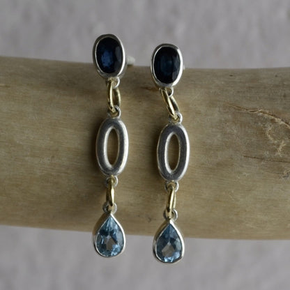 Silver earrings with blue gemstones on a wooden stick