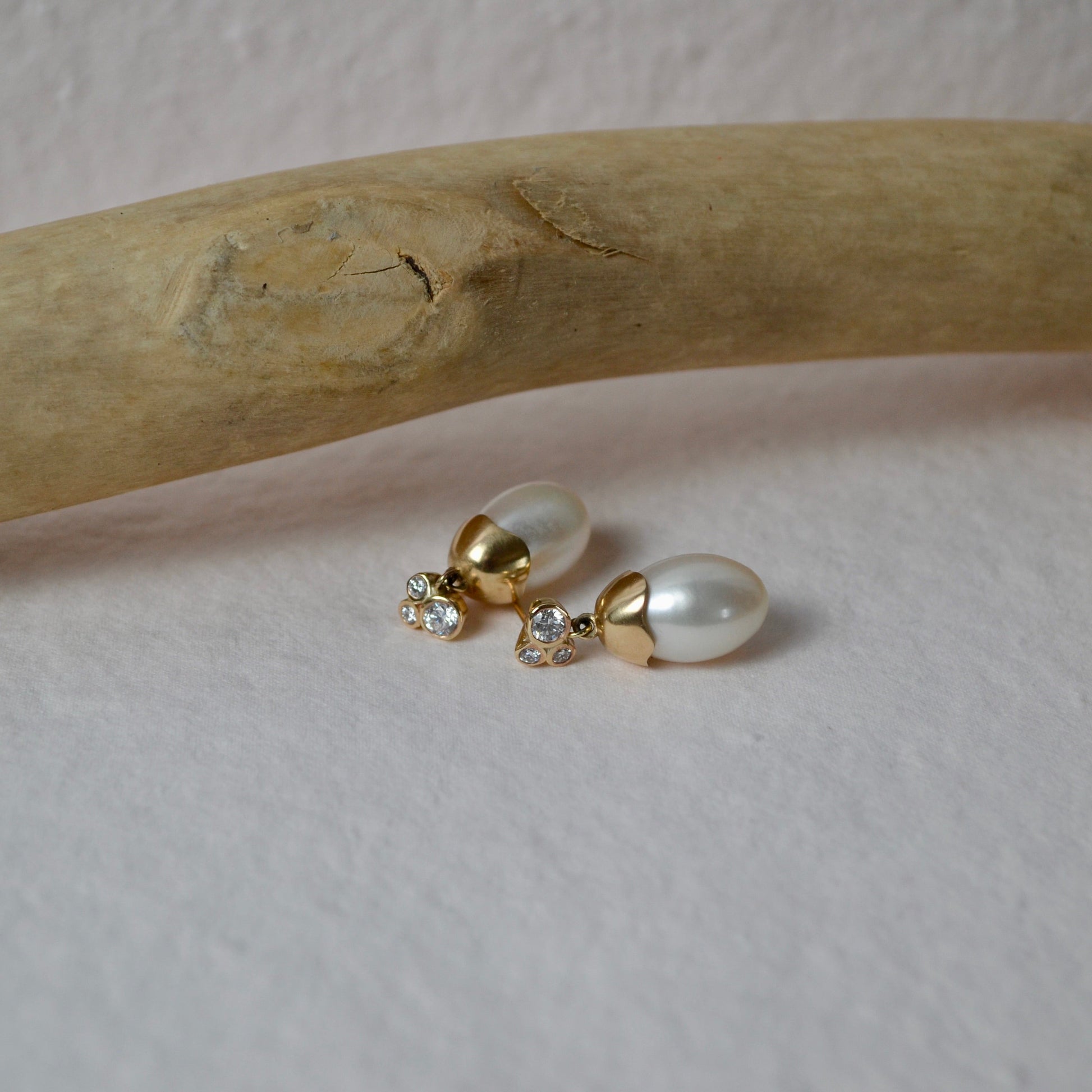 Pair of pearl earrings on a wooden stick with a neutral background