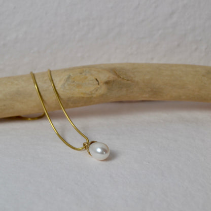 Gold earring with a pearl on a wooden stick against a white background
