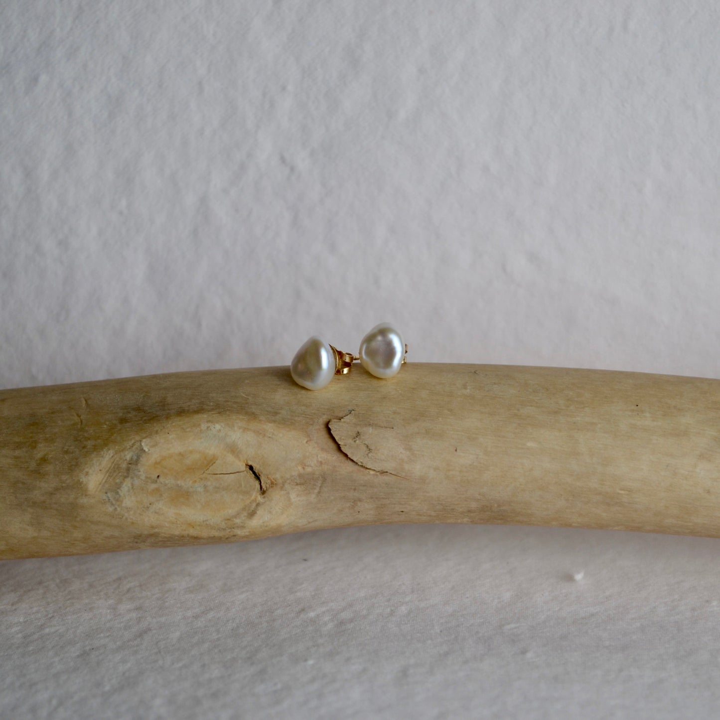 Pair of pearl earrings on a piece of driftwood against a plain background