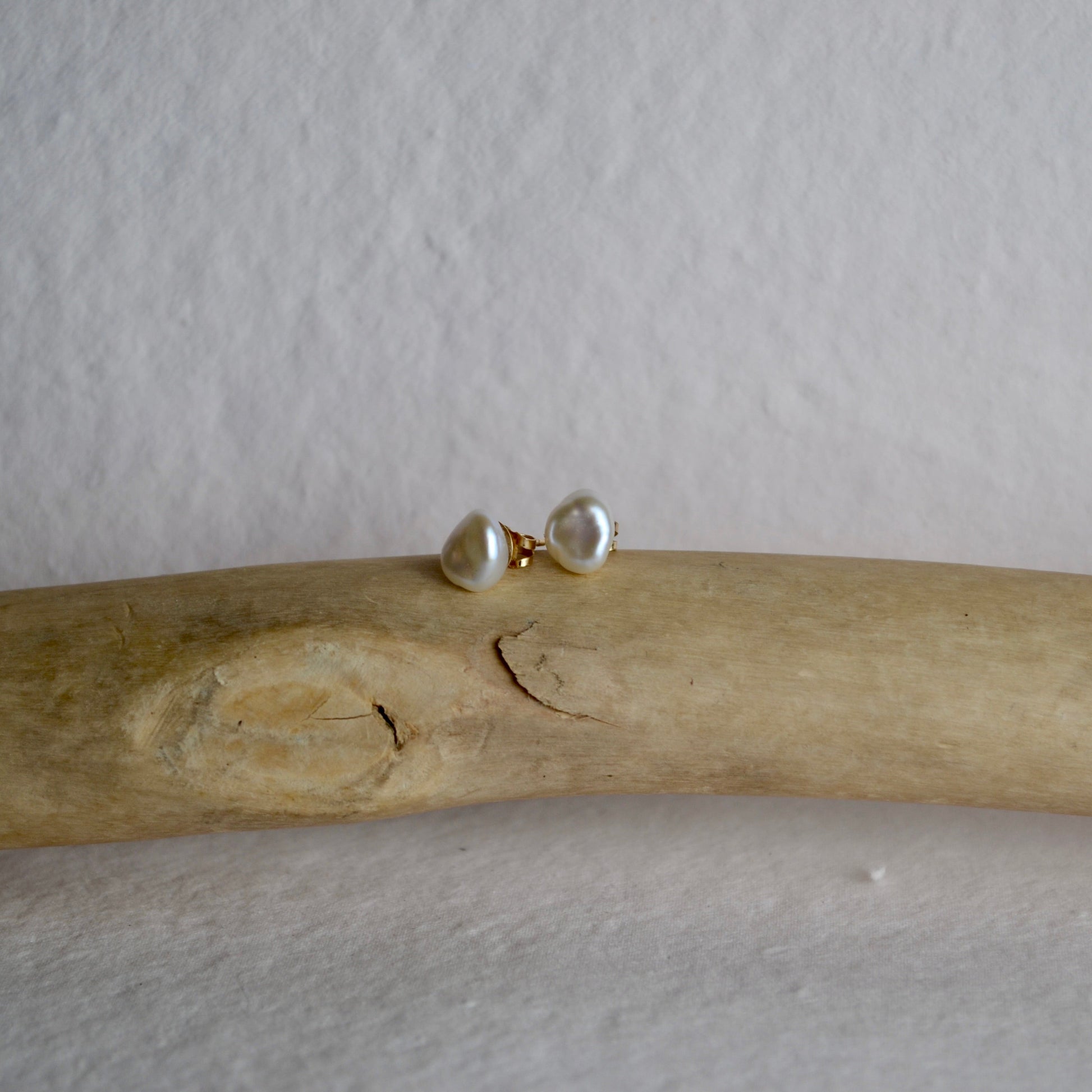 Pair of pearl earrings on a piece of driftwood against a plain background
