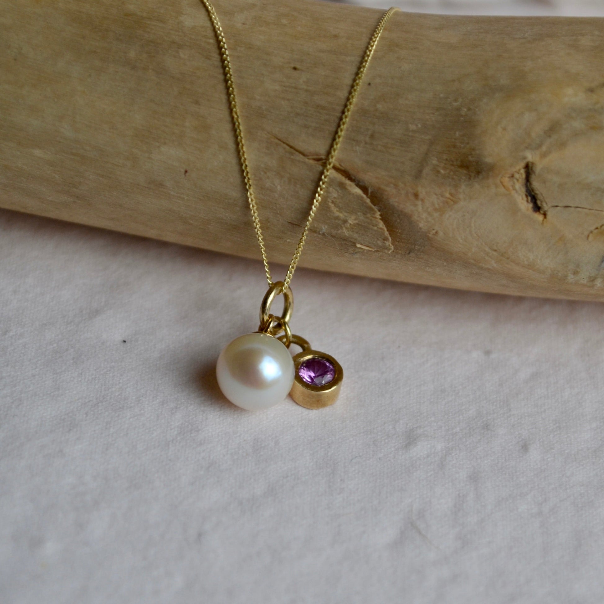 Gold necklace with a pearl and gemstone pendant on a wooden surface