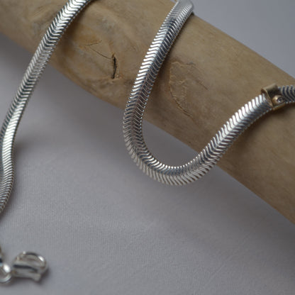Silver snake chain necklace on a wooden stick with a neutral background