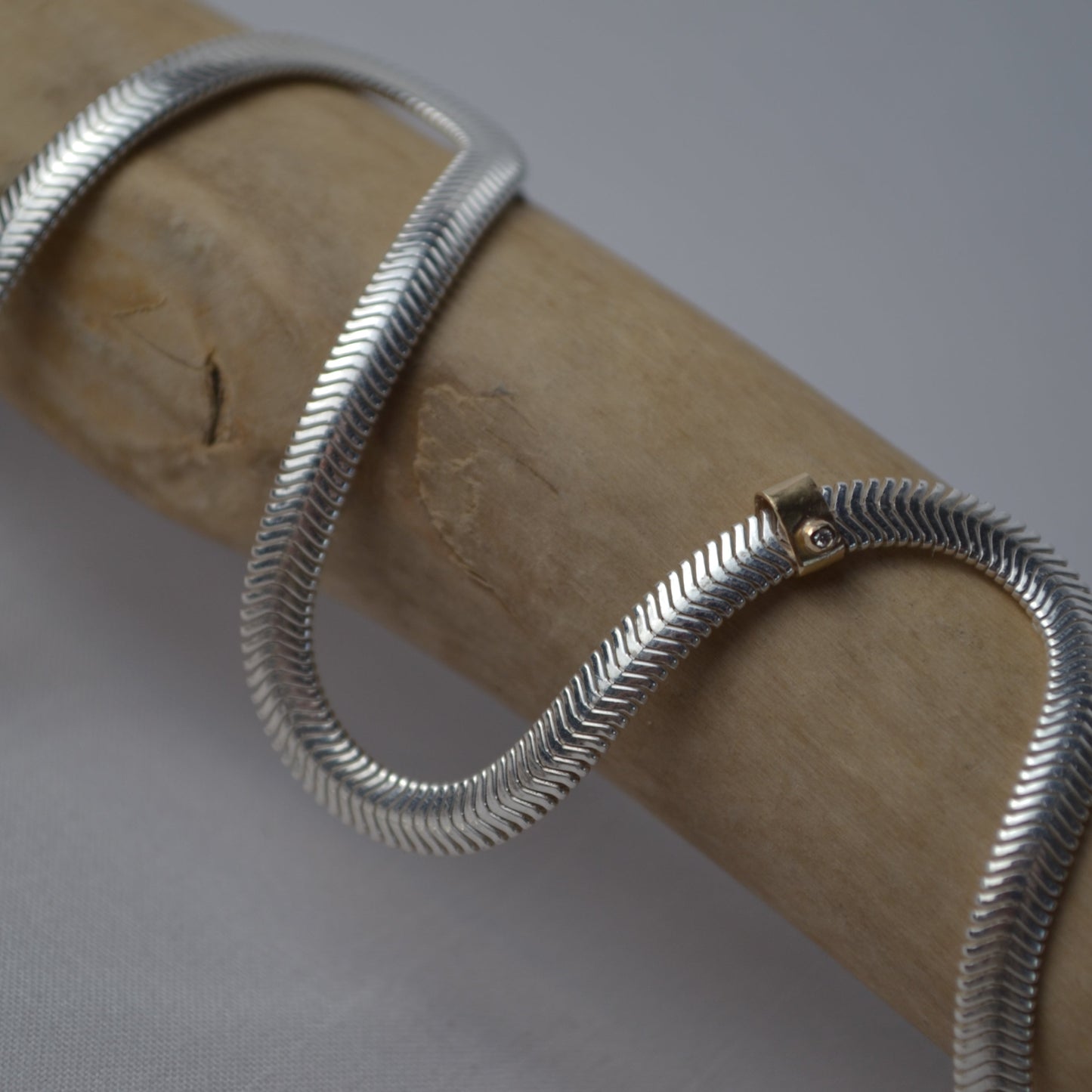 Silver snake chain necklace on a wooden stick against a gray background