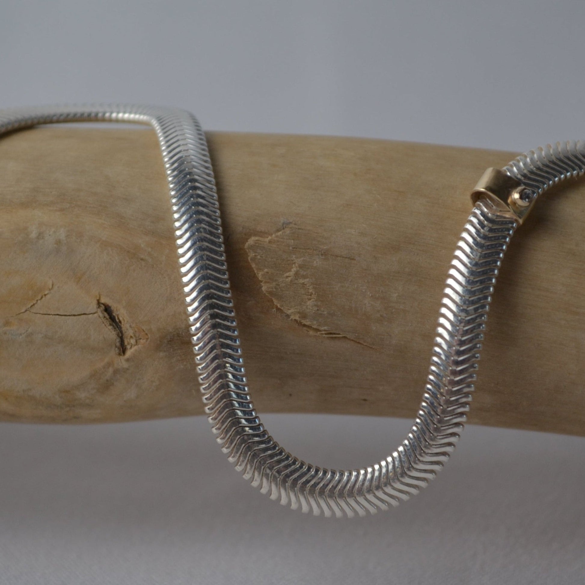 Silver snake chain necklace on a wooden block with a gray background