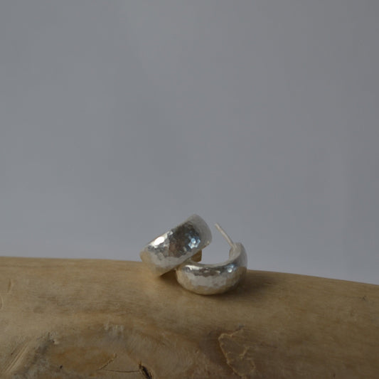 Silver hoop earrings on a textured surface with a neutral background
