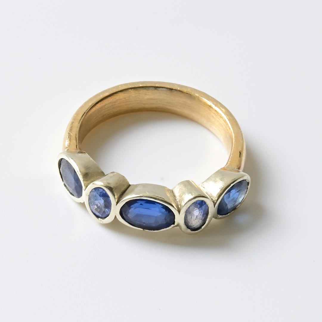 A yellow gold band engagement ring with alternate pale and dark blue sapphires set in white gold.
