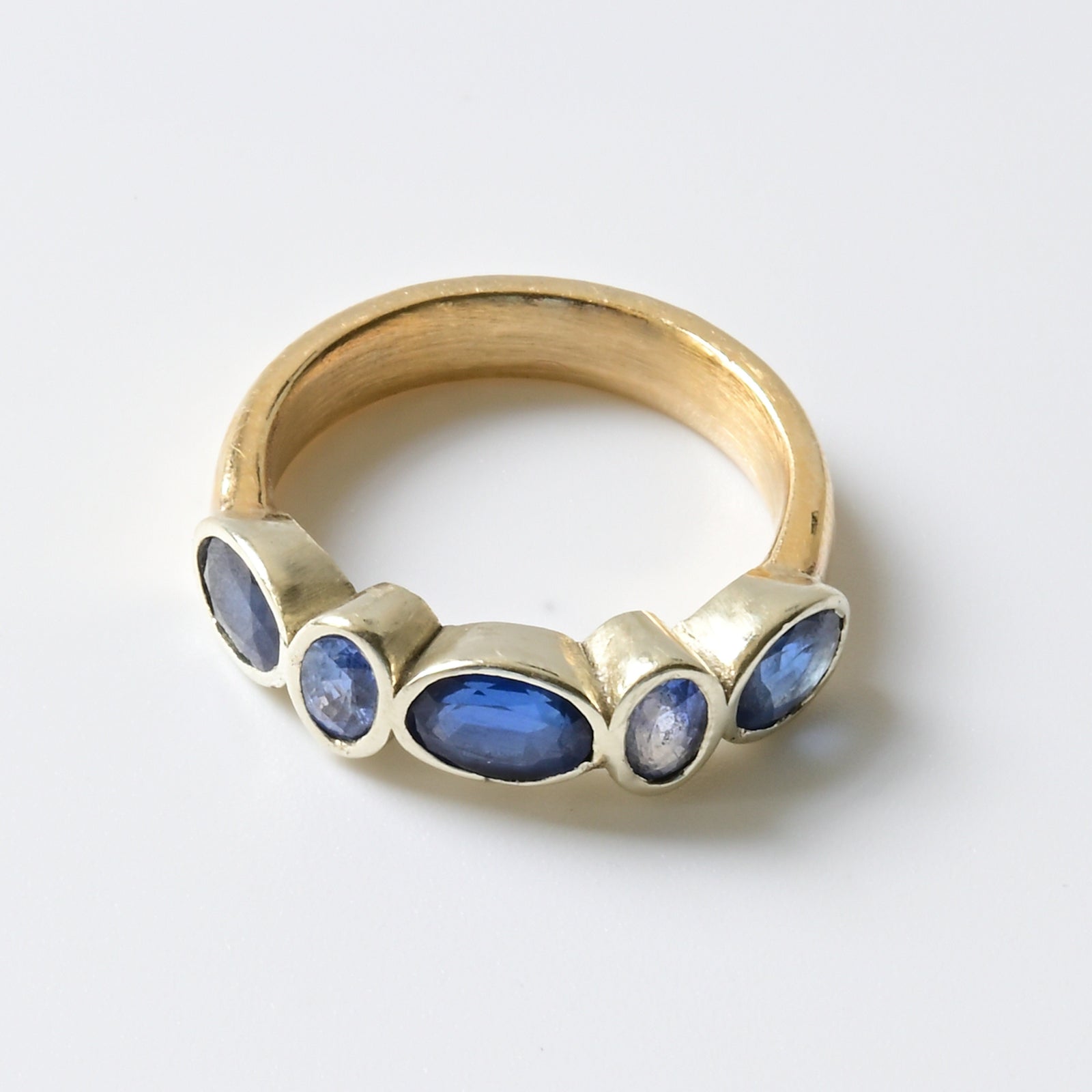 A yellow gold band engagement ring with alternate pale and dark blue sapphires set in white gold.