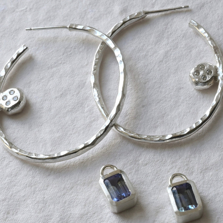 A pair of tanzanite and sterling silver hoops with diamond photographed on white. Handmade fine jewellery by Madeleine.