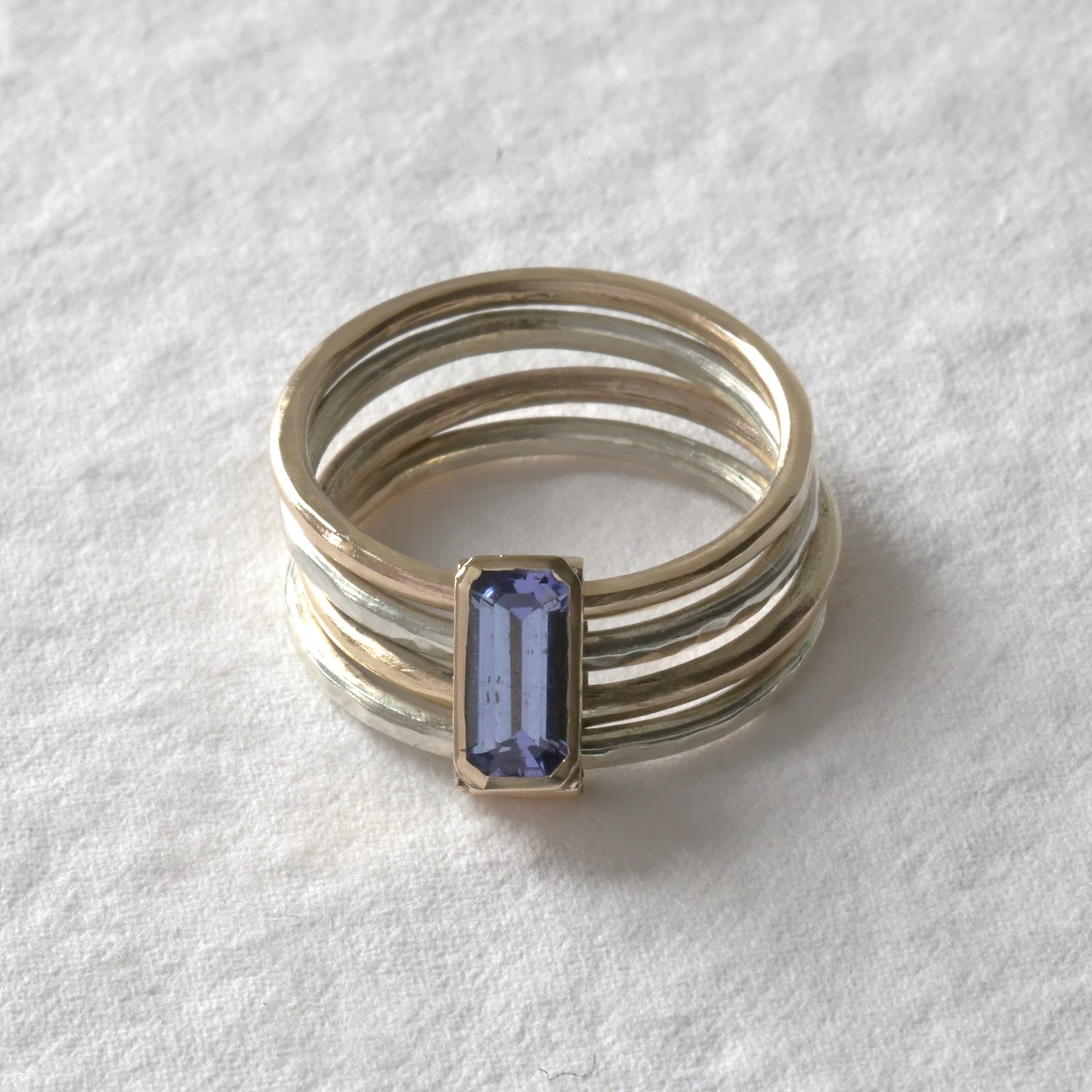 A stack of four gold rings, with the top ring featuring an octagon-shaped tanzanite gemstone.