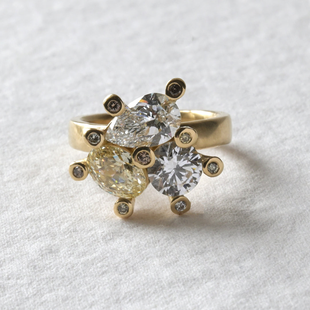An 18ct yellow gold engagement ring with a central cluster of three uniquely shaped diamonds, surrounded by smaller yellow diamonds set in claws.