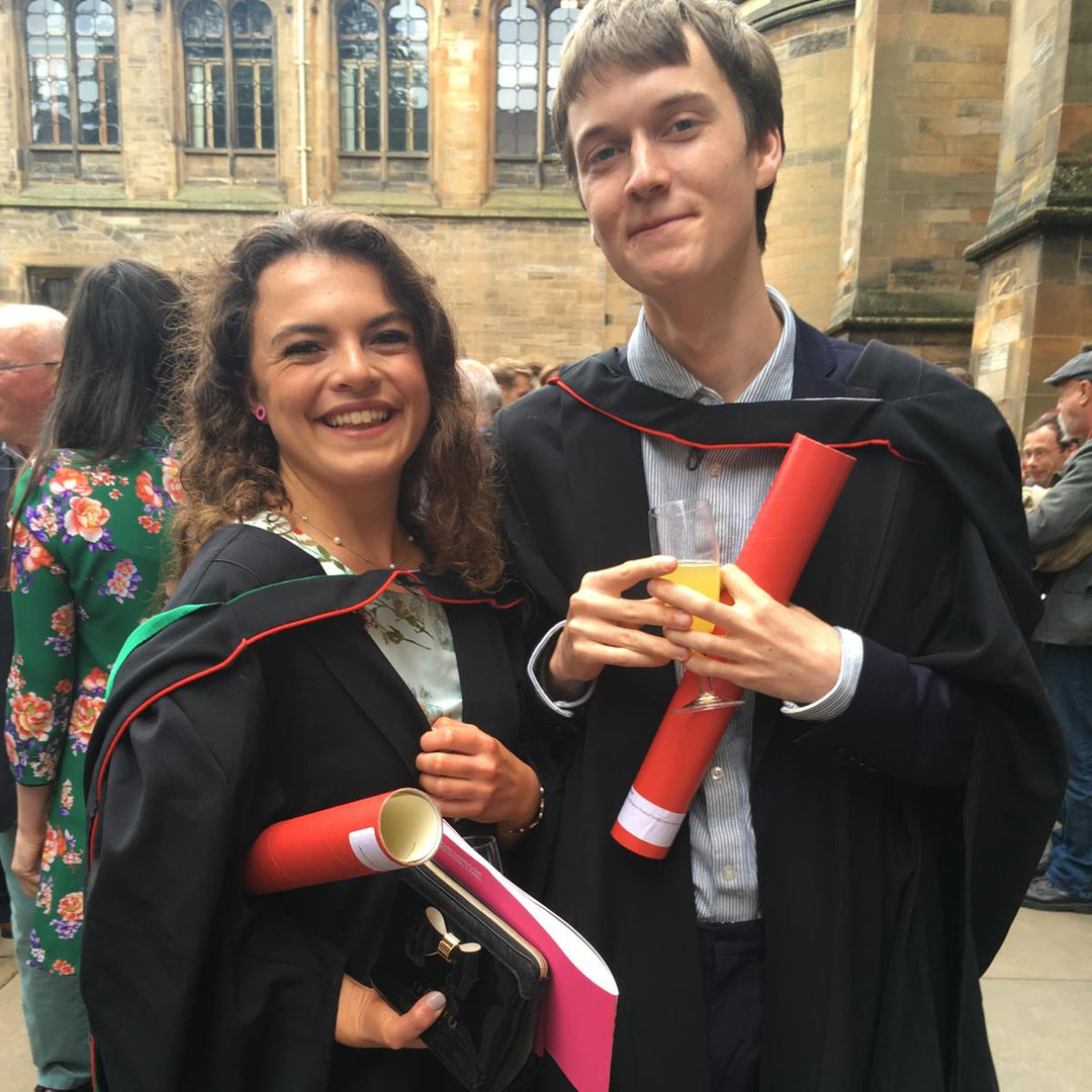 Two individuals in graduation gowns standing outdoors with a building in the background