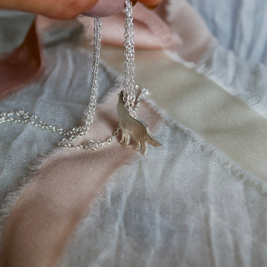 Hand holding a silver necklace with a small animal pendant on a light fabric background